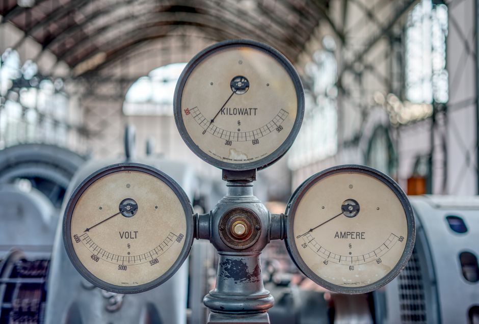 Close-up of vintage volt, ampere, and kilowatt gauges in an old industrial setting.